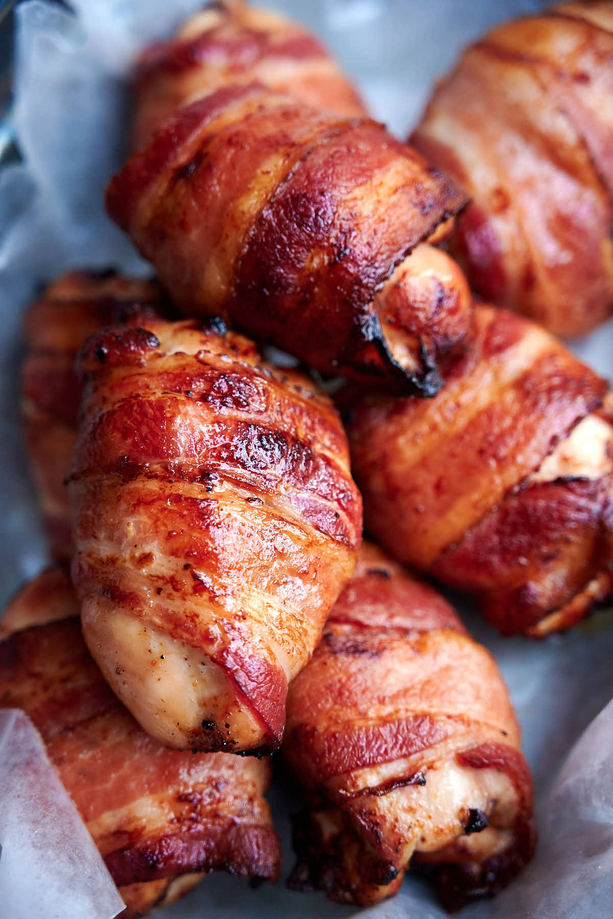 Chicken thighs wrapped in bacon, cooked, in basket lined with white wax paper.