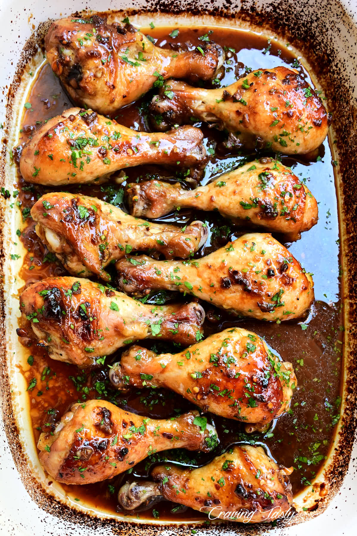 Top down view of baked chicken drumsticks in a large white baking dish with red sauce on the bottom.