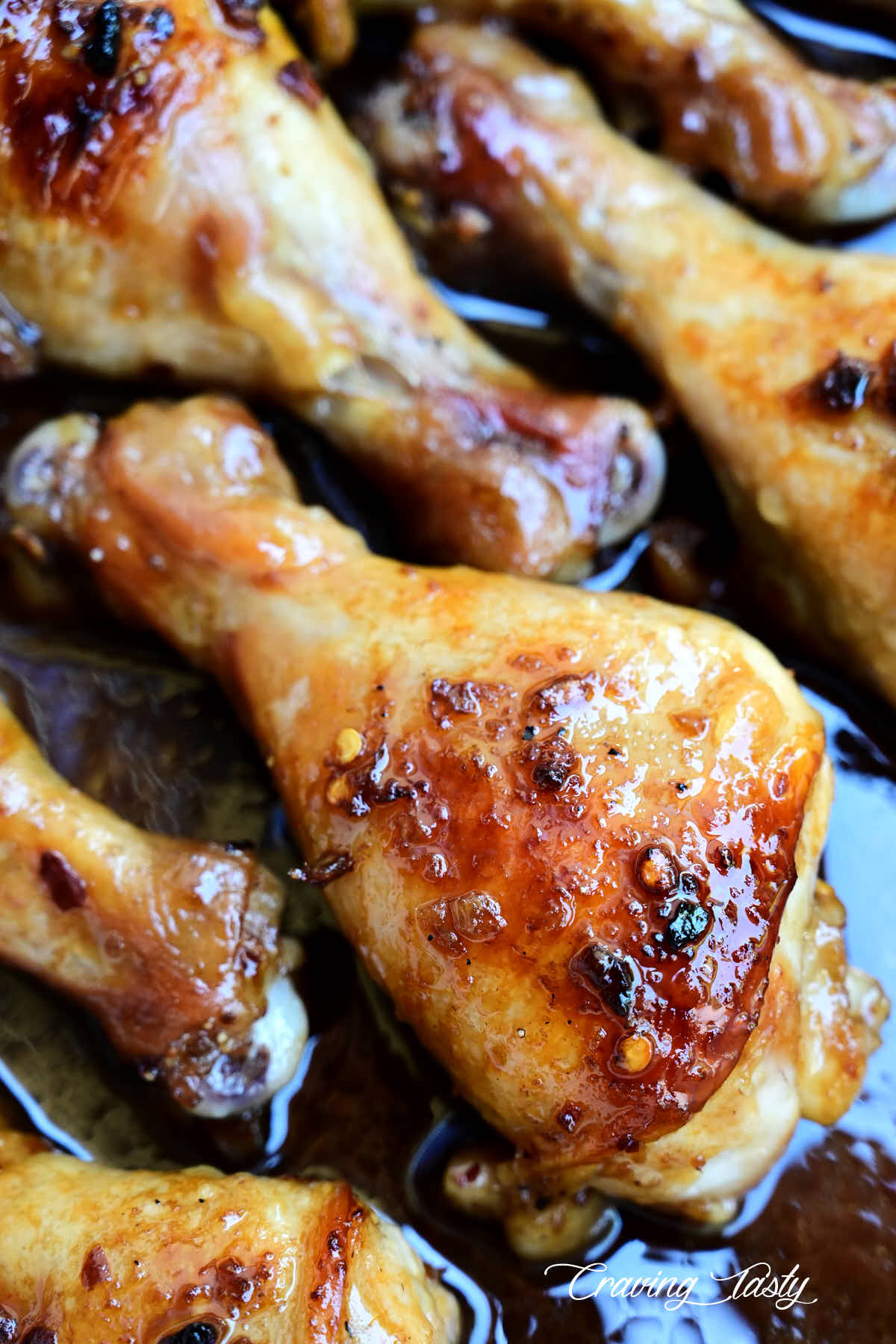 Close up of golden brown baked chicken drumstick in a white baking dish with red sauce on the bottom.