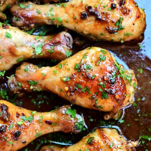 A large, juicy, crispy baked chicken drumstick, inside a pan with sauce, surrounded by partial chicken legs.