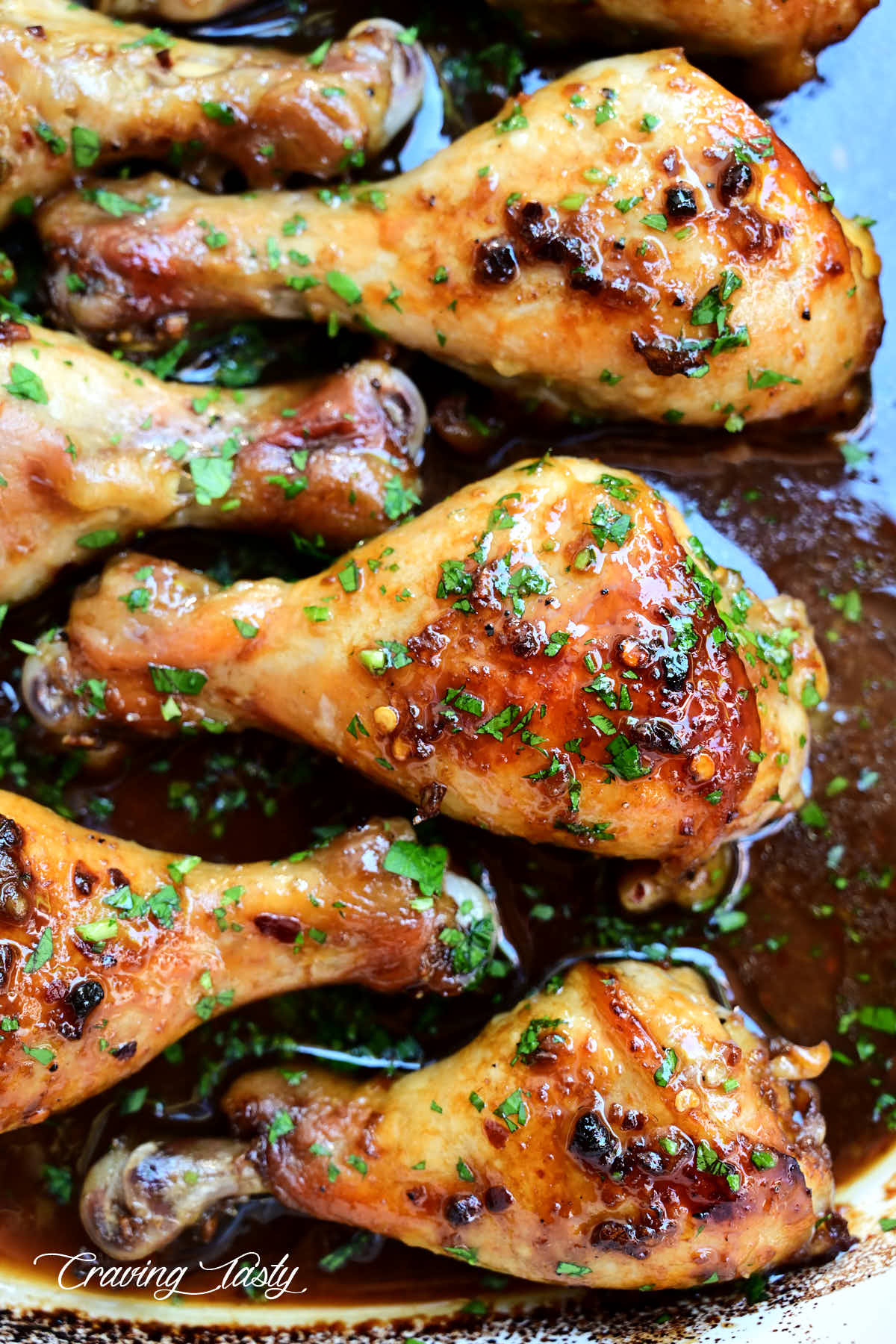 A large, juicy, crispy baked chicken drumstick, inside a pan with sauce, surrounded by partial chicken legs.