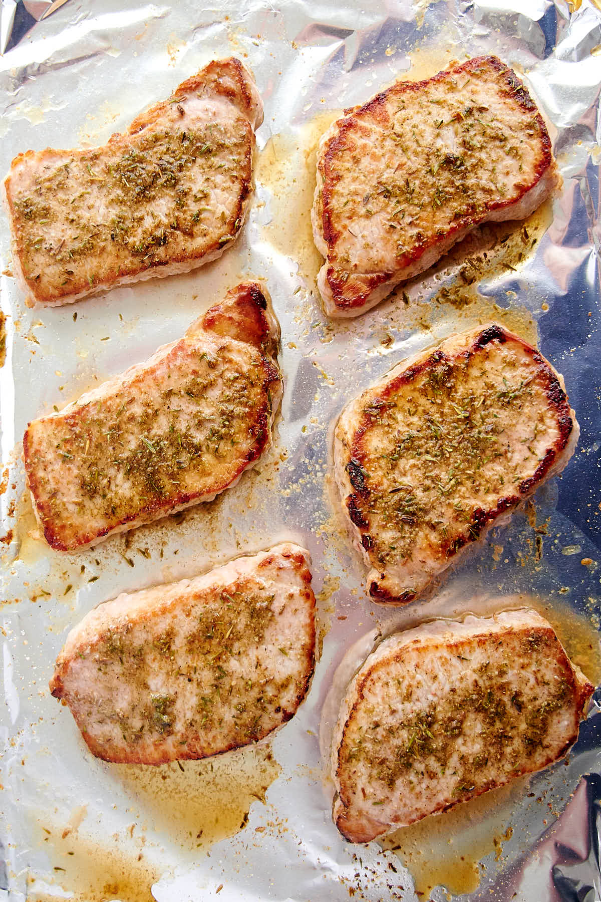 Six baked pork chops on a baking pan lined with foil.