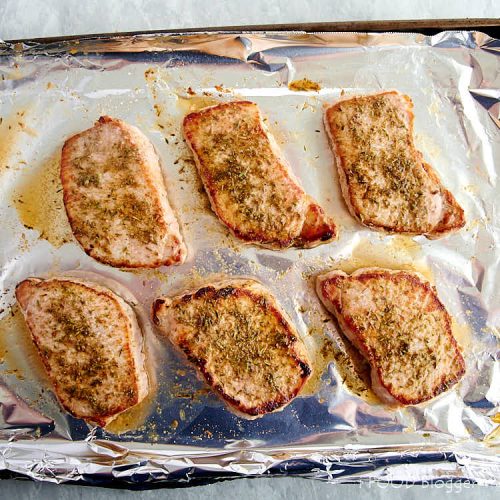 Pork chops on a baking sheet, fully cooked.
