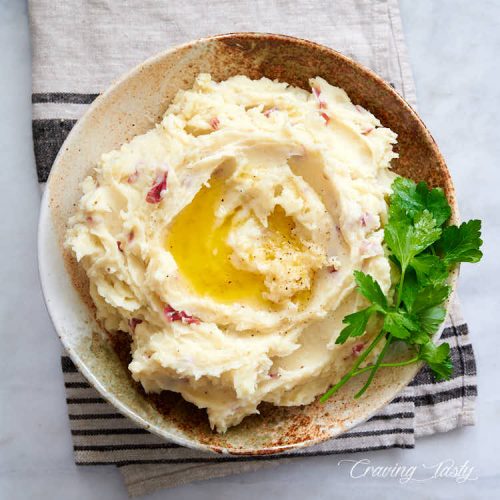 Top down view of a bowl with mashed red potatoes, garnished with twigs of fresh parsley.