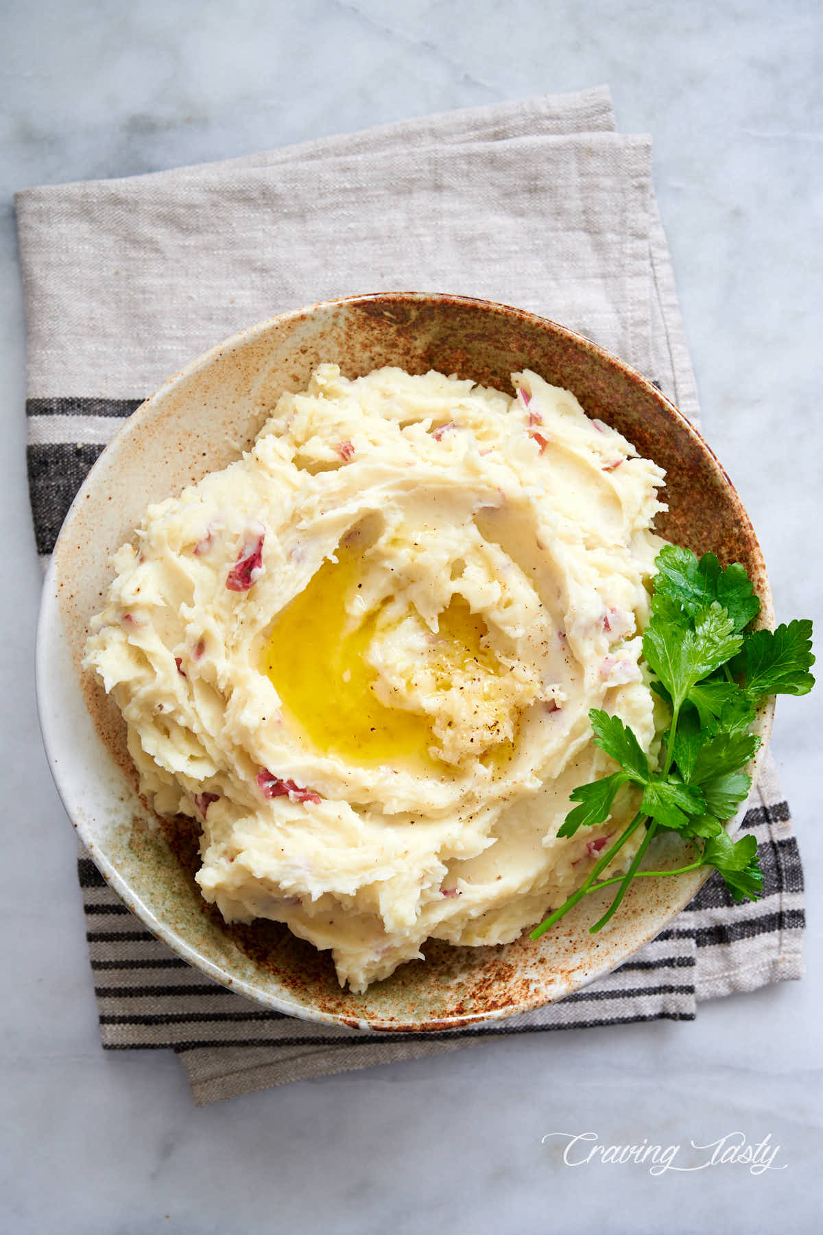 Top down view of a bowl with mashed red potatoes, garnished with twigs of fresh parsley.