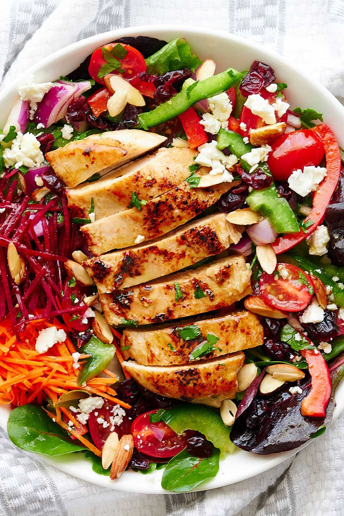 Grilled chicken breast, on a bed of garden mix, chopped peppers, tomatoes, red onions on the sides, all on a white plate.