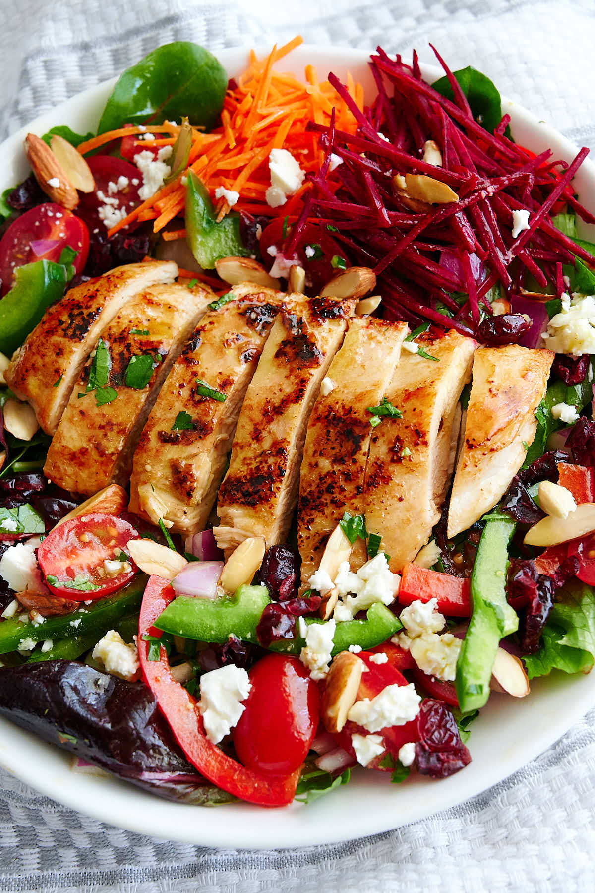 45 degree view of a white bowl with a grilled chicken breast on top a bed of garden vegetables and garden mix.