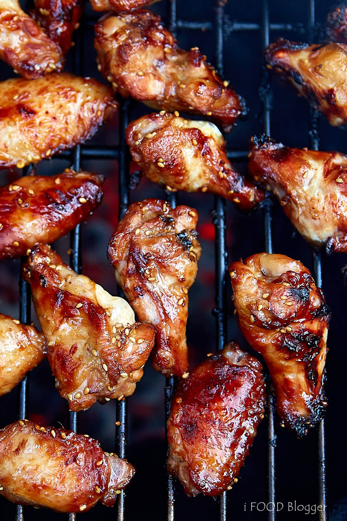 Top down view of grilled chicken wings, fully cooked, crispy and browned, on a grill grate over a bed of charcoal.