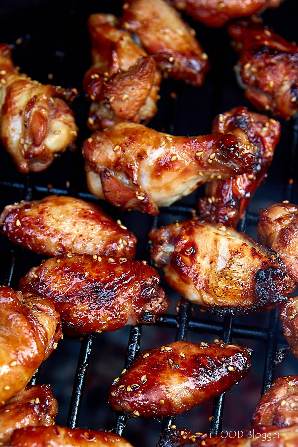 Grilled chicken wings, fully cooked, crispy and browned, on a grill grate over a bed of charcoal.