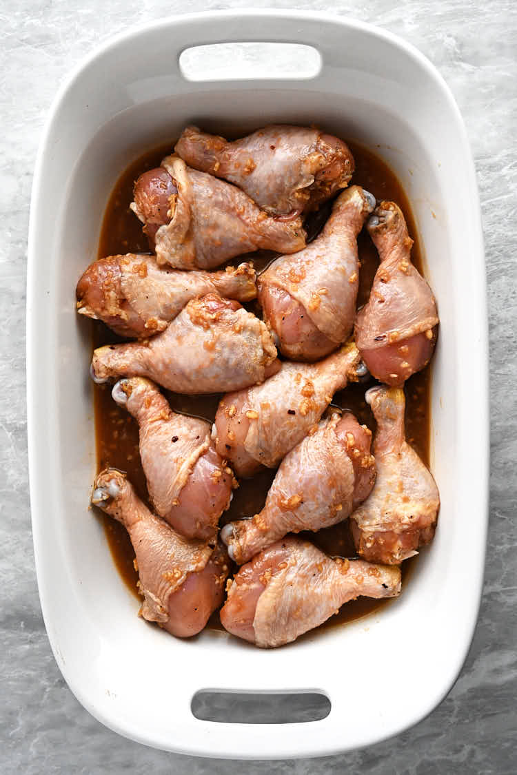 Raw chicken legs, with the honey garlic marinade, inside a long white baking dish.