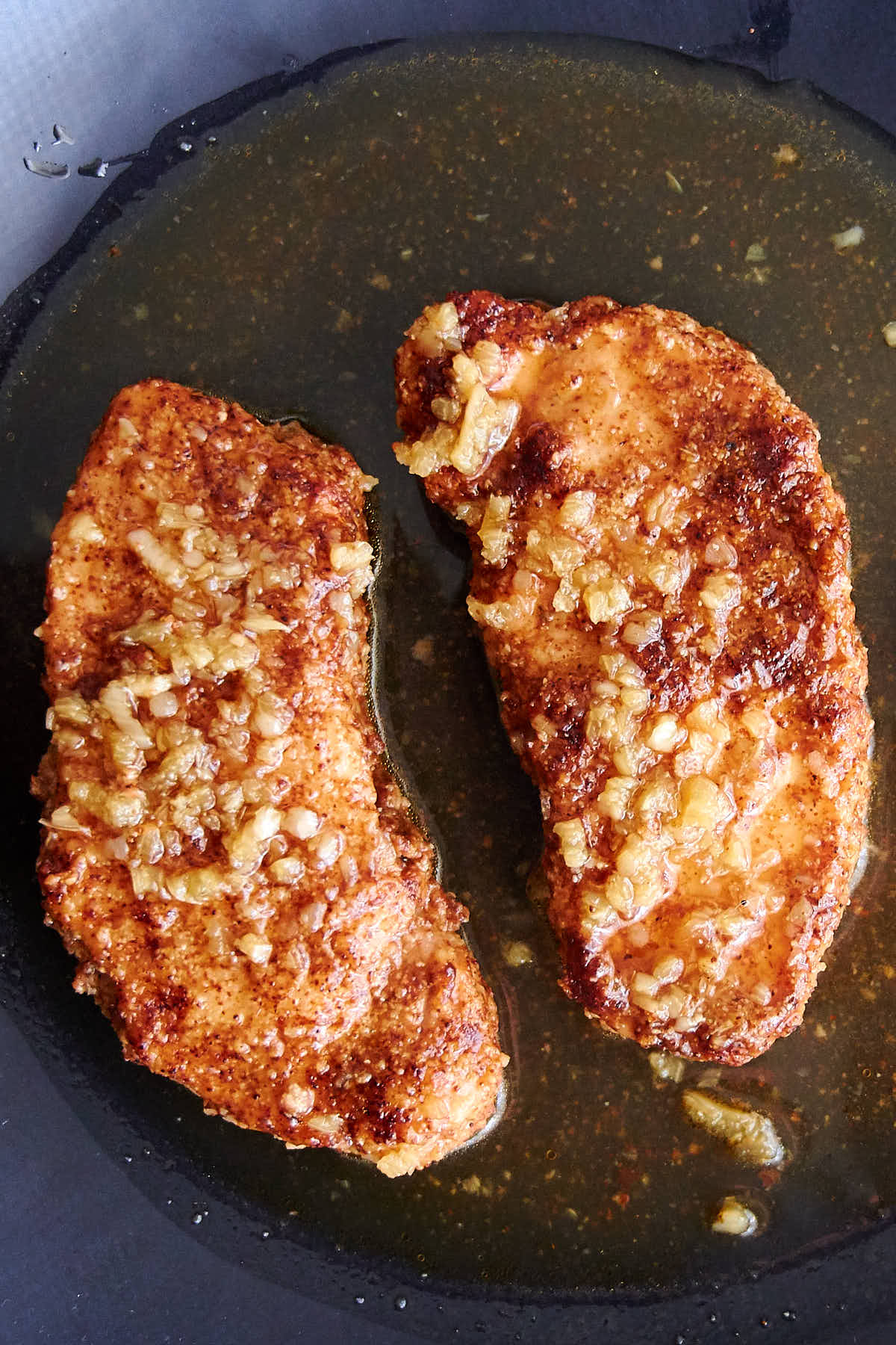 Two honey garlic pork chops, cooked in Instant Pot, on a black plate in sauce.