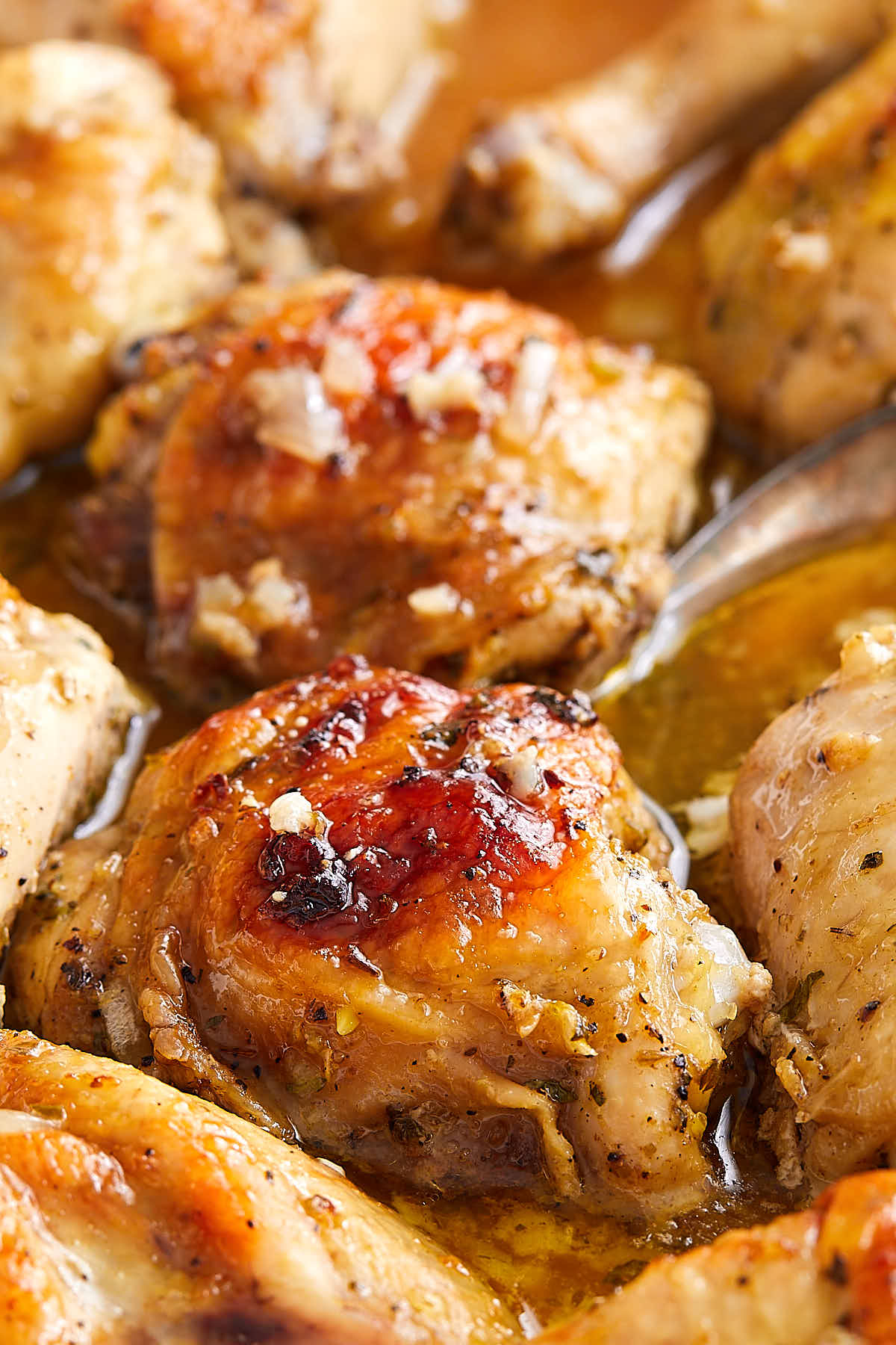 A close up of browned roasted mojo chicken inside a baking dish, with amber mojo sauce at the bottom.