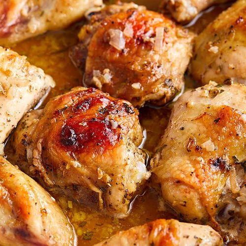 Close up of roasted mojo chicken in a white baking dish.