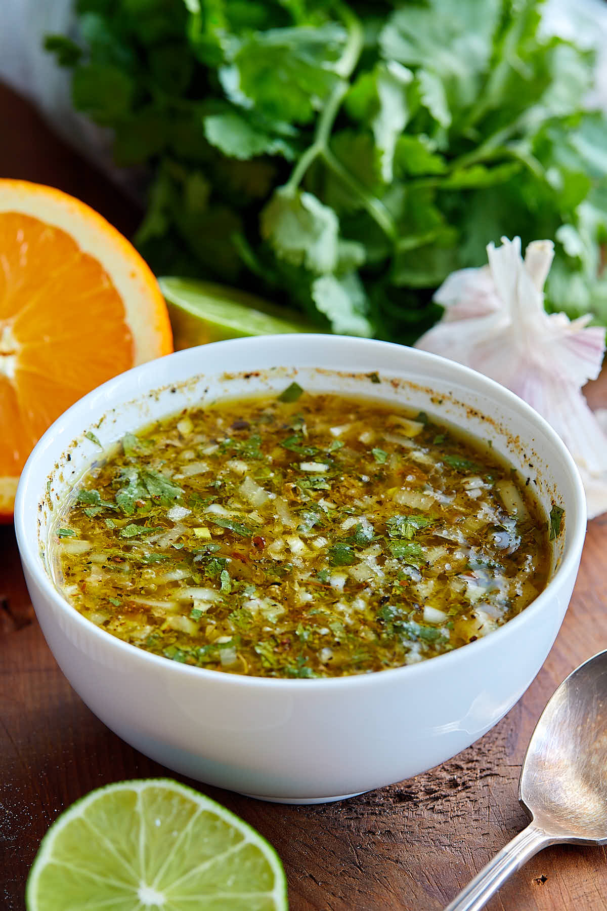 Cuban mojo marinade in a white bowl, surrounded by parsley, garlic, cut lime and orange.