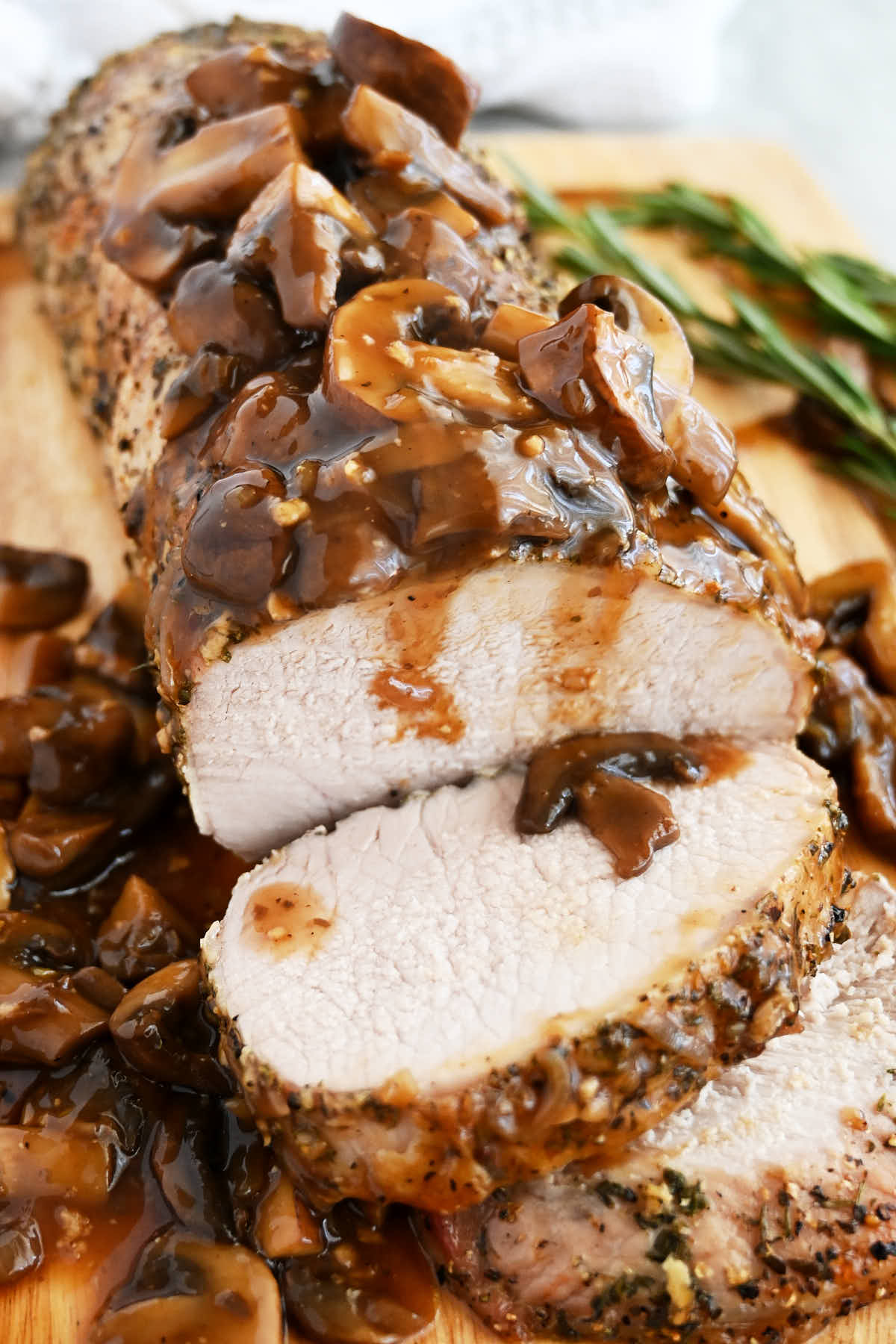 Roasted pork loin, on a cutting board, mushroom sauce on top.