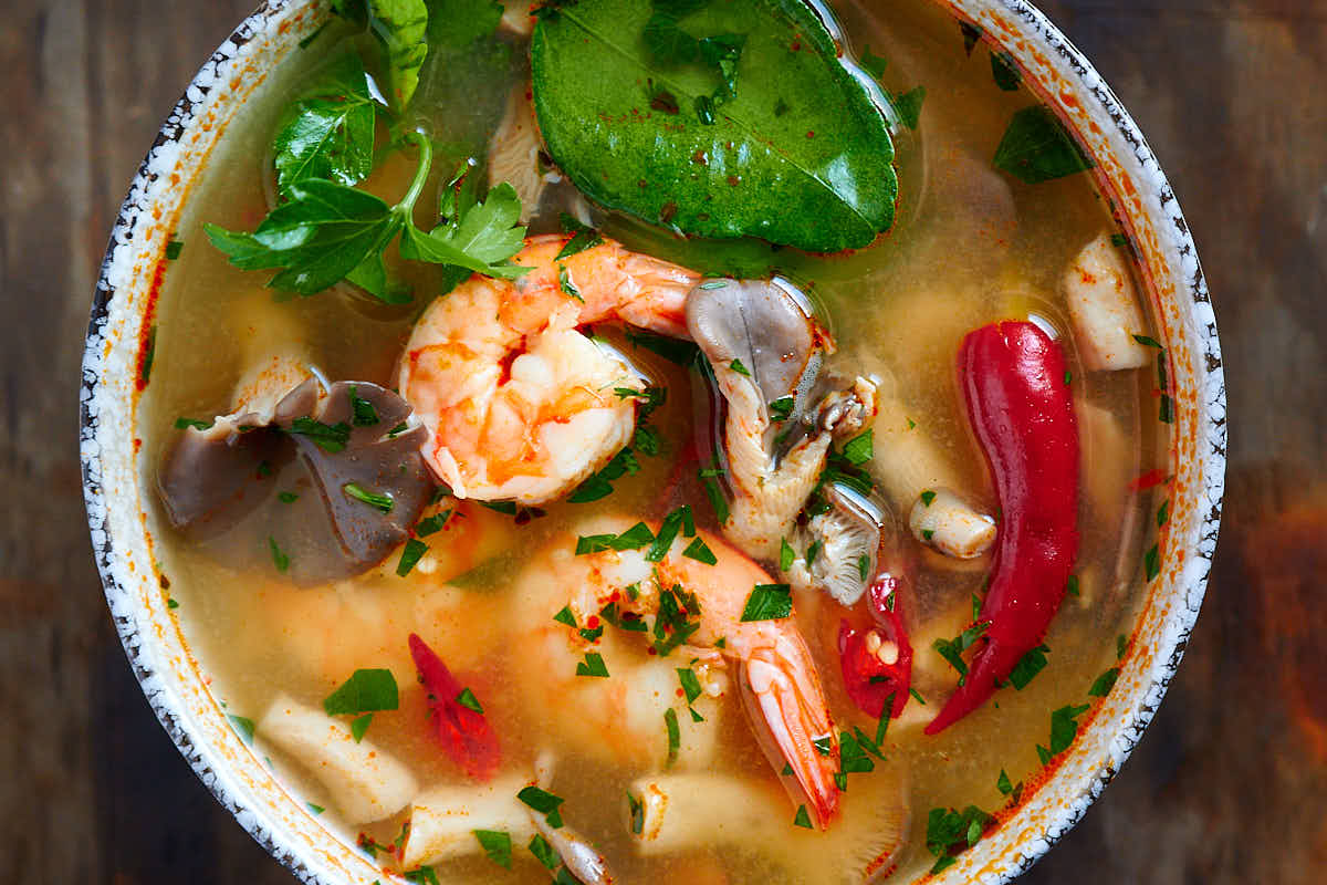 Top down view of Thai Tom Yum soup with plump shrimp, oyster mushrooms, bird eye chilies, lime leaves and cilantro.