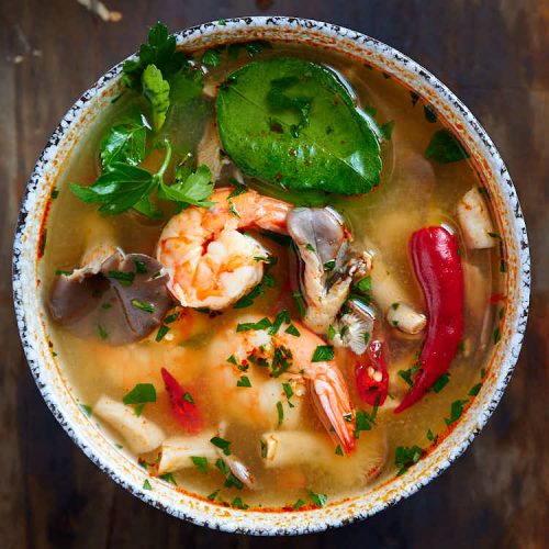Top down view of Thai Tom Yum soup with plump shrimp, oyster mushrooms, bird eye chilies, lime leaves and cilantro.