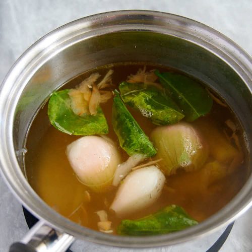 lemongrass, galangal, lime leaves and shallots in a pot with chicken stock.