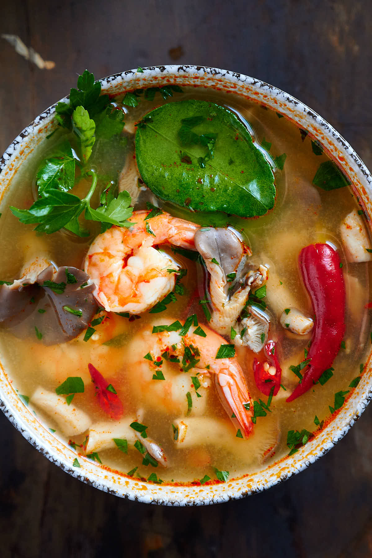 Top down view of Thai Tom Yum soup with plump shrimp, oyster mushrooms, bird eye chilies, lime leaves and cilantro.