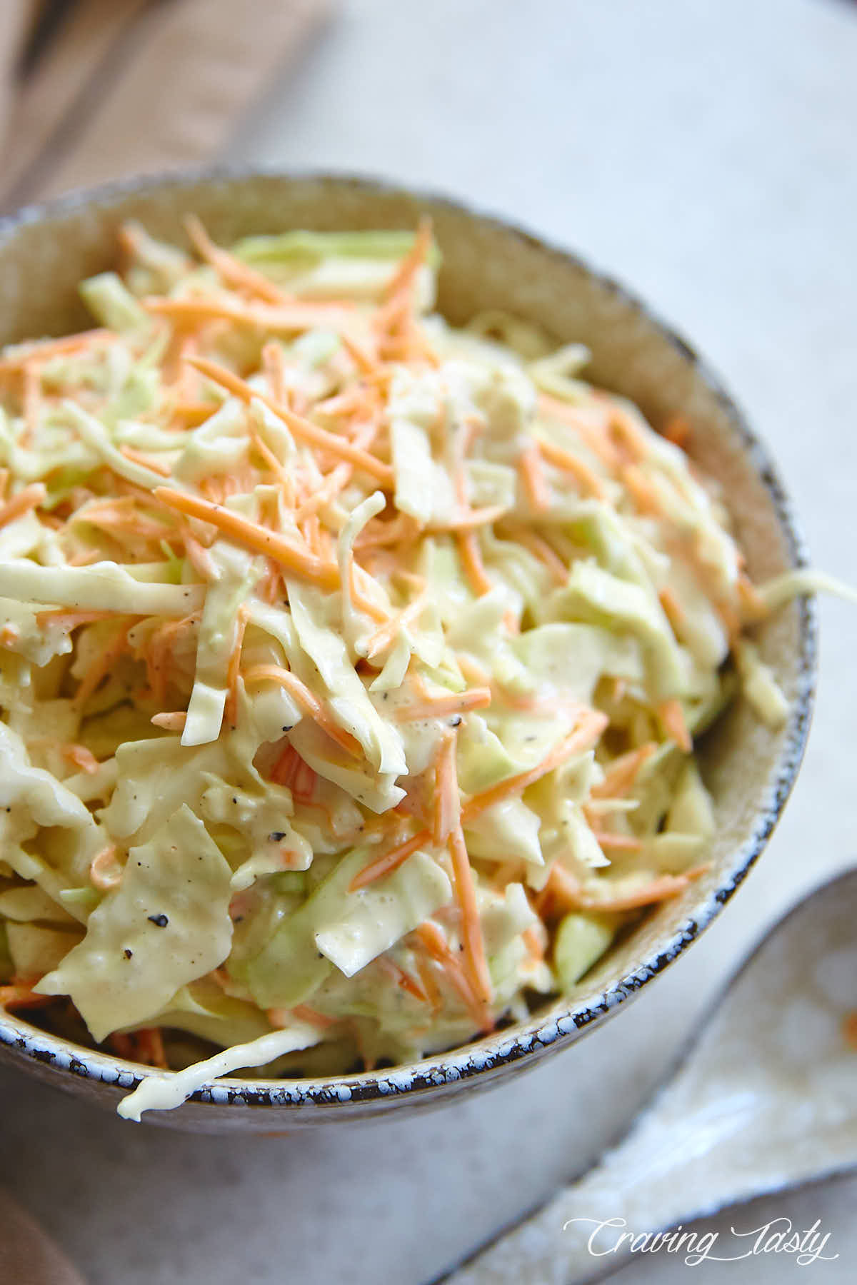 Homemade coleslaw inside a speckled grey bowl, on a table with a spoon next to the bowl.