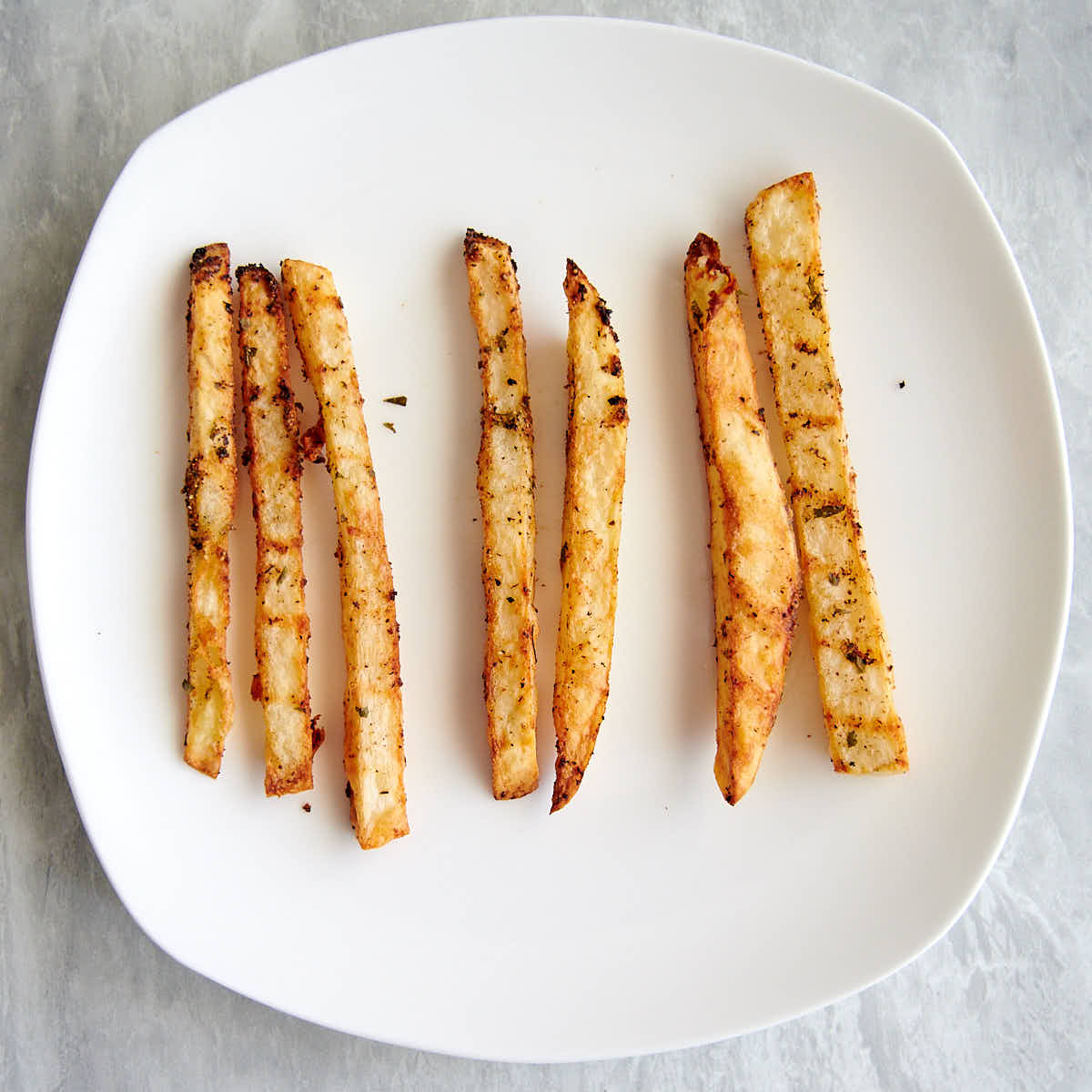 Three sets of air fried French fries of varying thickness on a white plate.