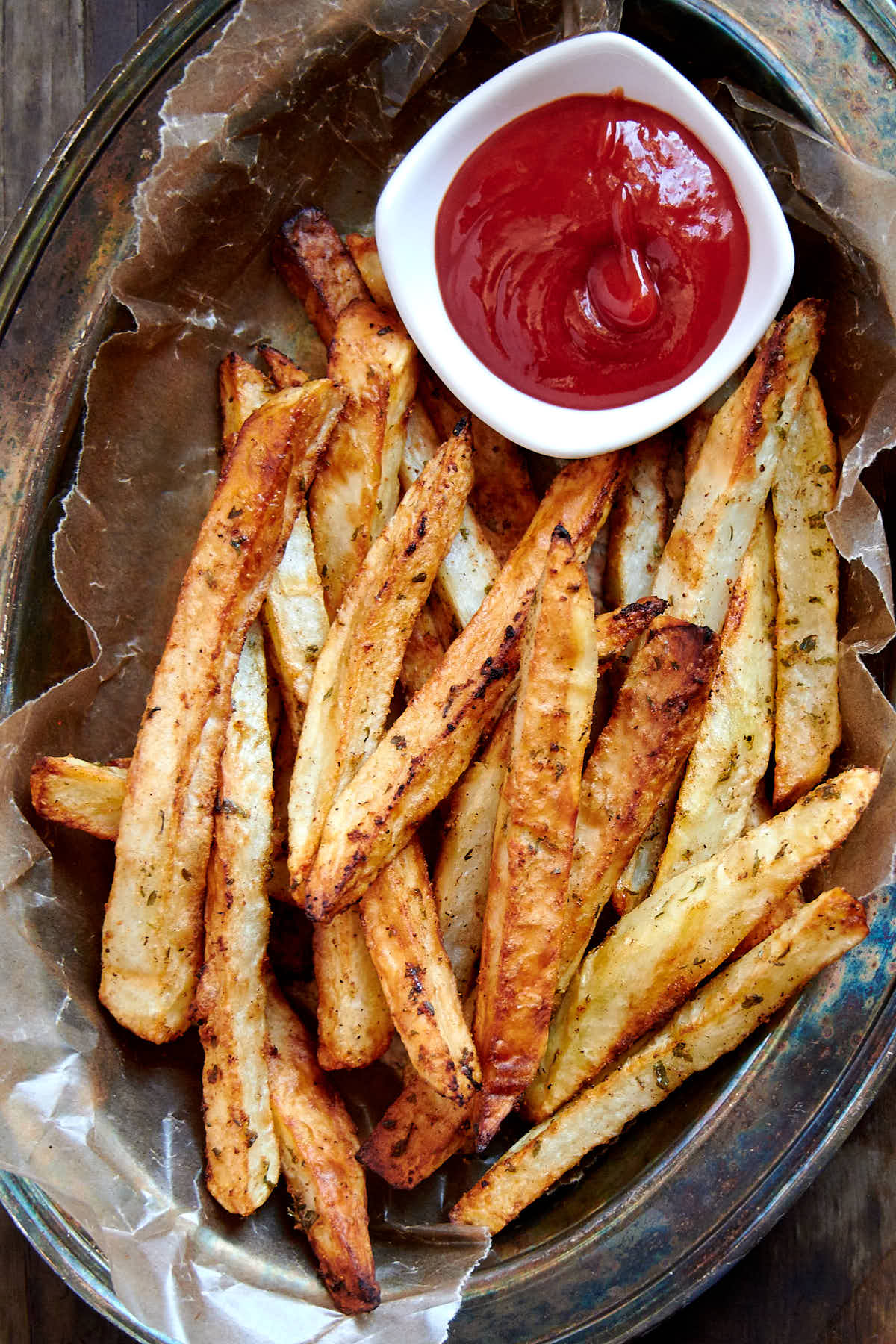 Close up of crunchy golden brown French fries in a serving basket with ketchup on the side.