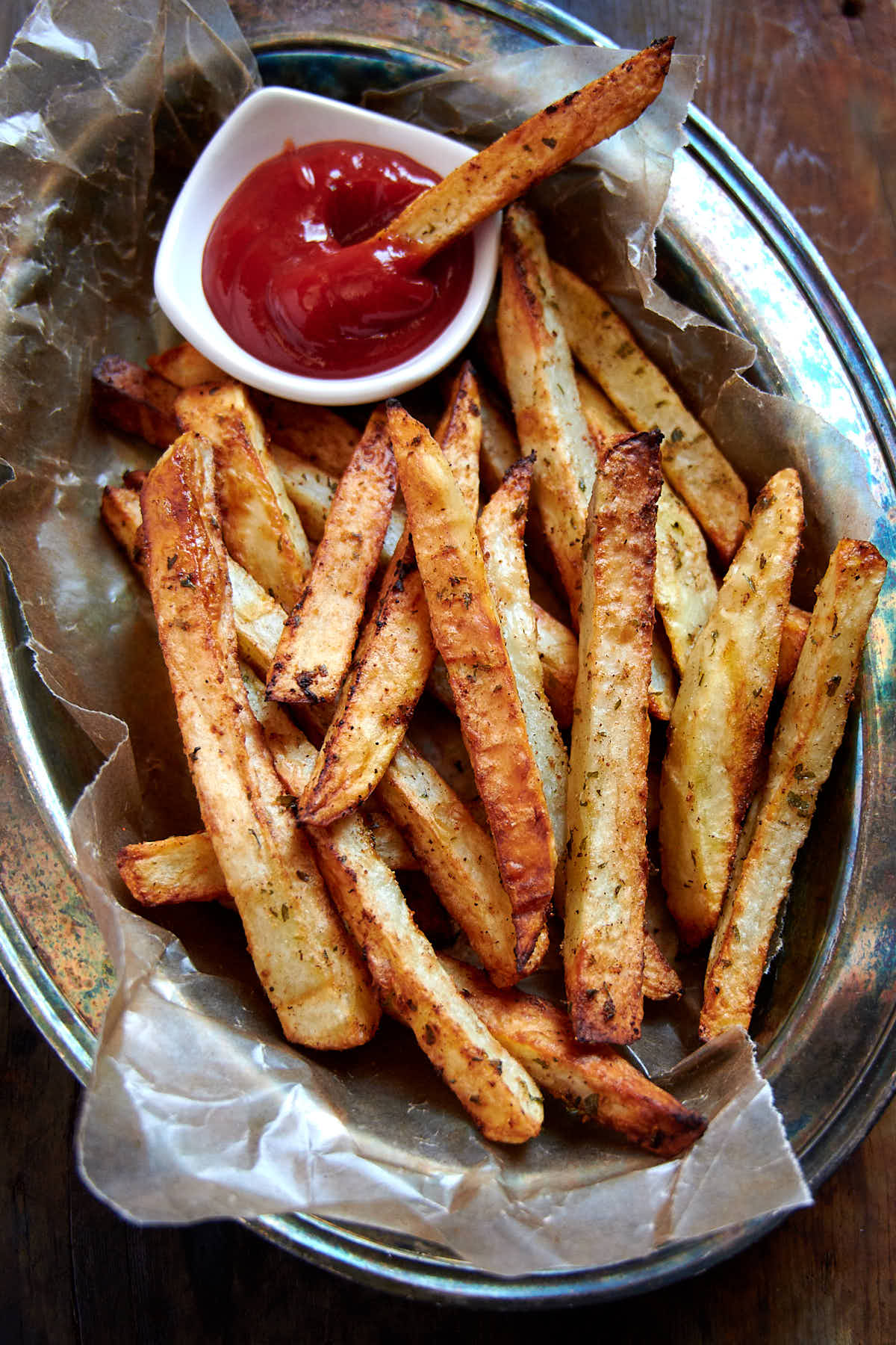 Crispy golden brown French fries in a basket lined with brown wax paper and a saucer with ketchup on the side.