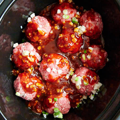 Raw meatballs in a slow cooker layered with sauce, green onions and water chestnuts.
