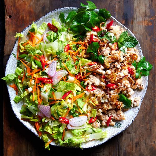 Thai larb gai - fried ground chicken, shredded cabbage, and fresh herbs on a round plate.