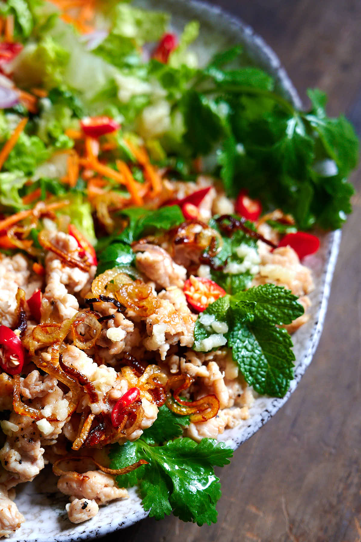 To view of larb gai - plate filled with shredded chicken, cabbage leaves, mint, basil and coriander leaves, sliced scallions and Thai red peppers, and seasoned with Thai dressing.