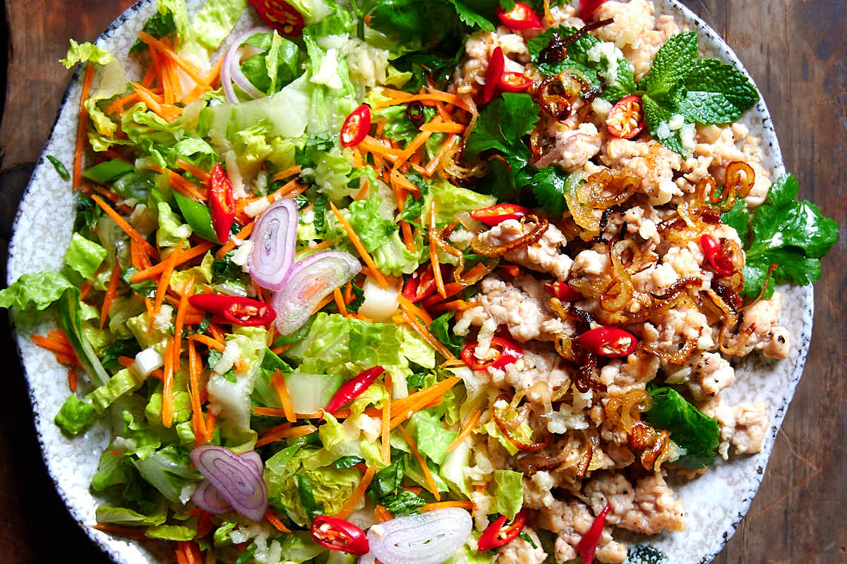 To view of larb gai - plate filled with shredded chicken, cabbage leaves, mint, basil and coriander leaves, sliced scallions and Thai red peppers, and seasoned with Thai dressing.
