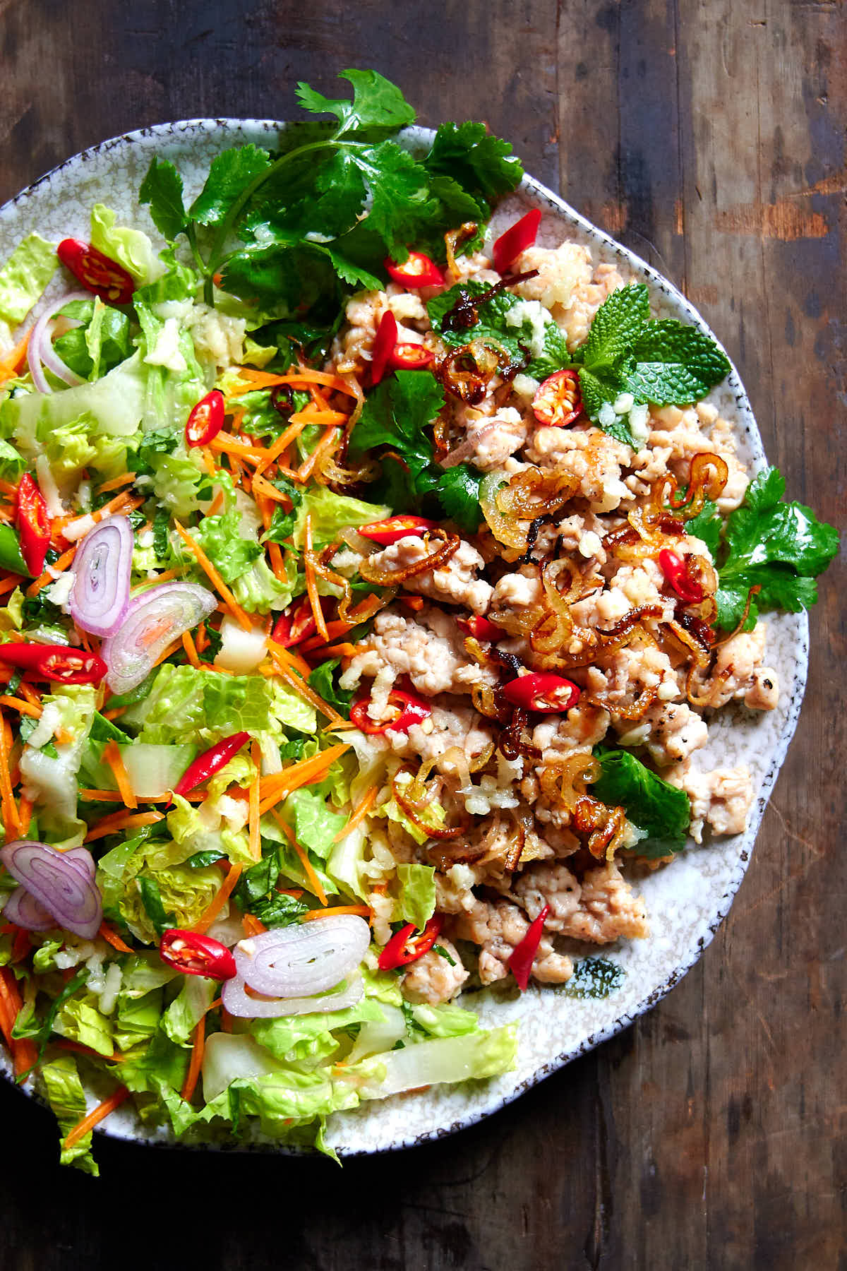 Thai chicken larb on a grey speckled plate - chicken, fresh herbs and chile peppers.