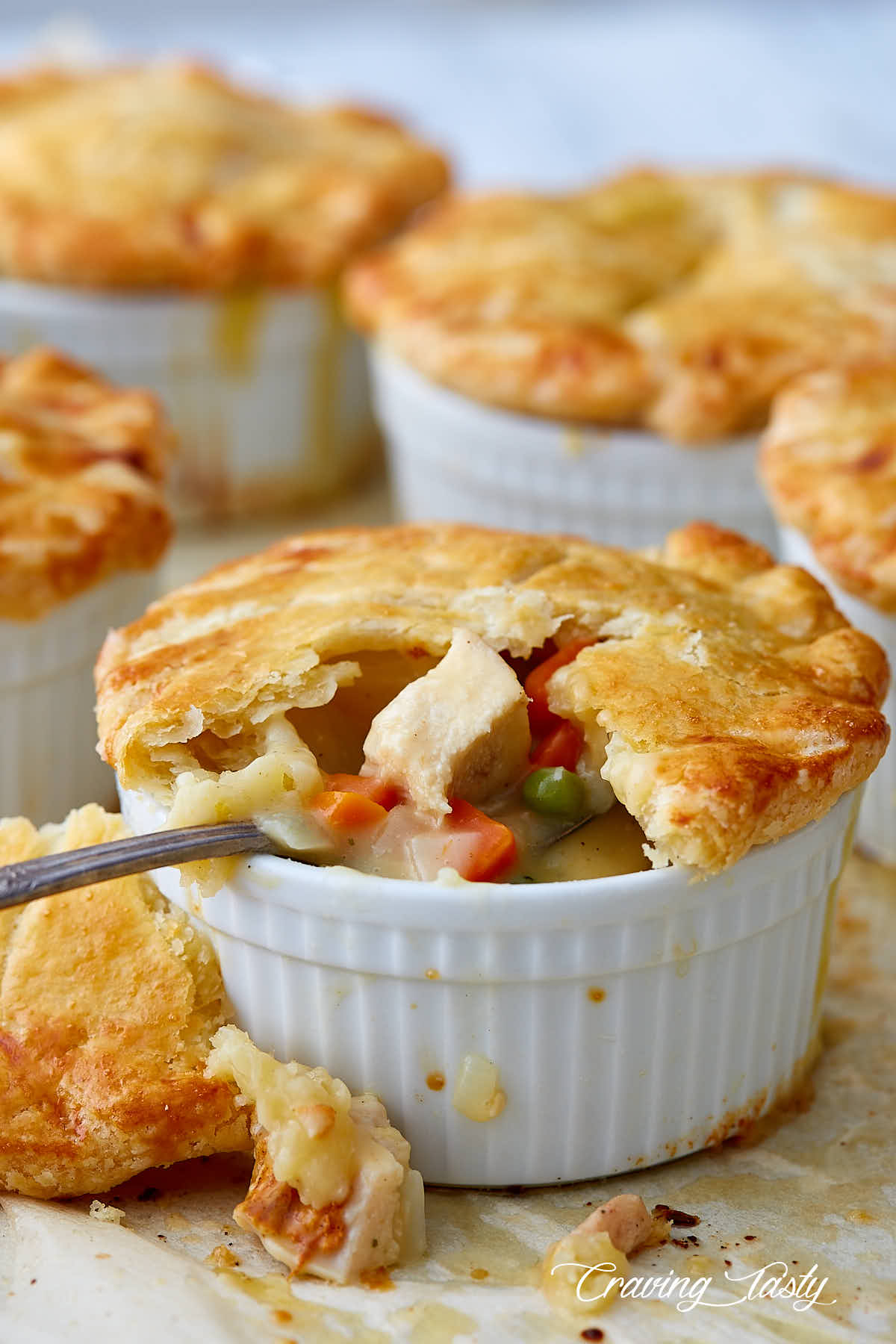 Several chicken pot pies on a baking dish, with the pie on the forefront split open and a spoon inserted into filling.