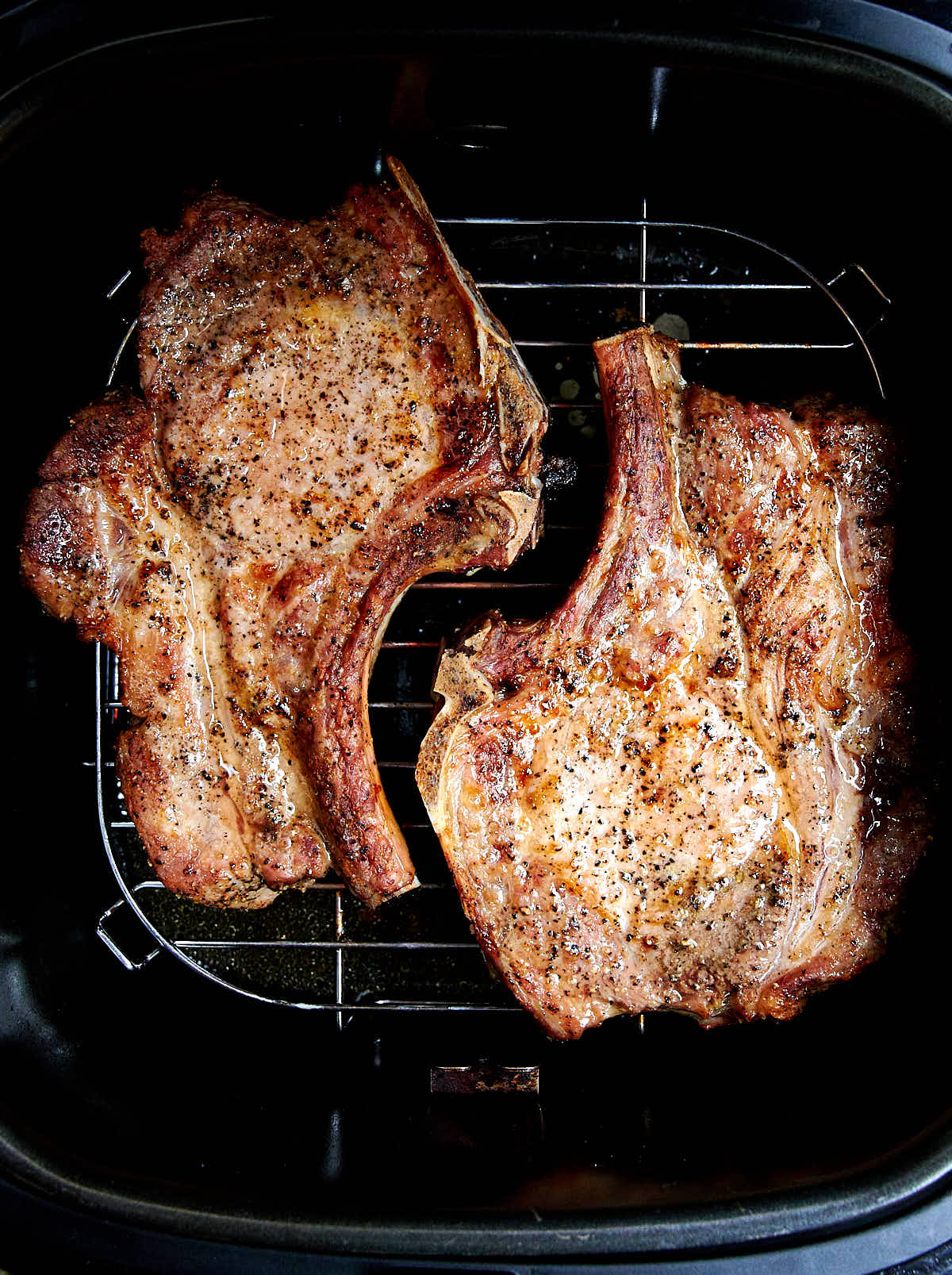 Two golden-brown pork chops on a rack in an air fryer.