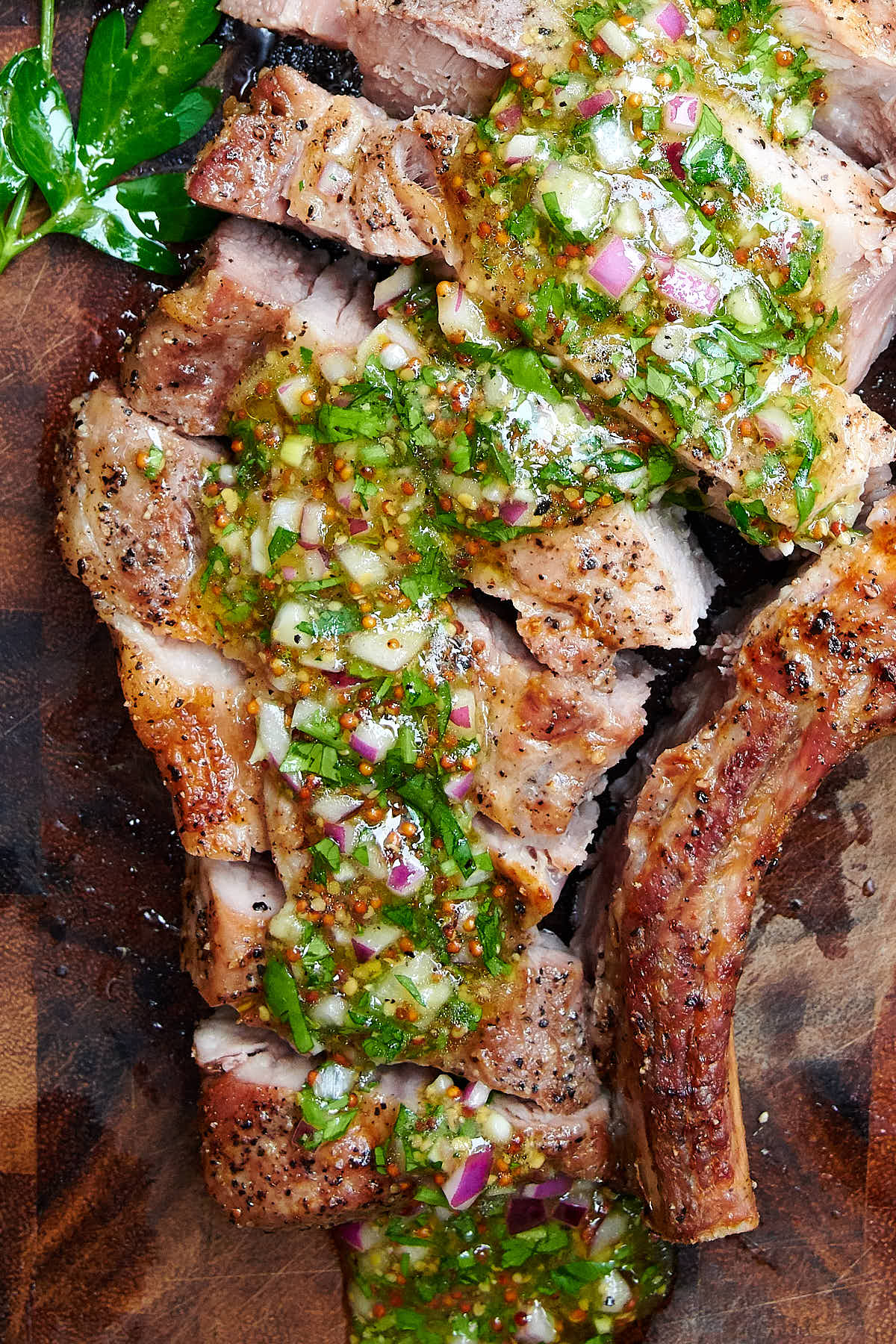 Close up of an air fryer pork chop on a cutting board, topped with mustard chimichurri sauce.