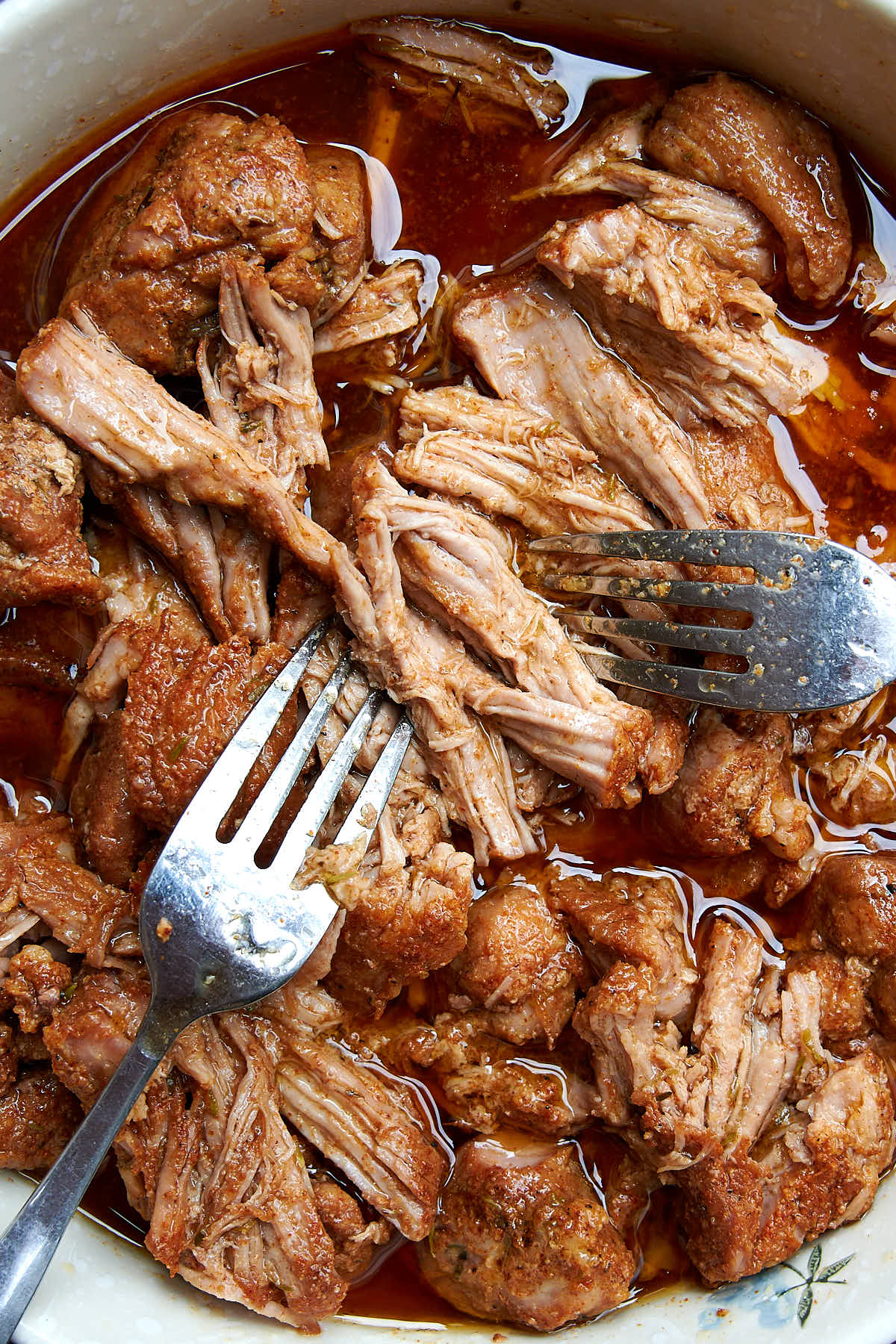 Pork being pulled apart in a bowl with amber juices.