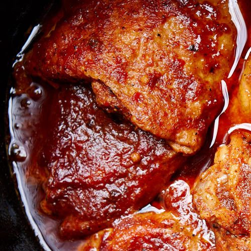 Pieces of chicken covered in BBQ sauce inside a slow cooker.