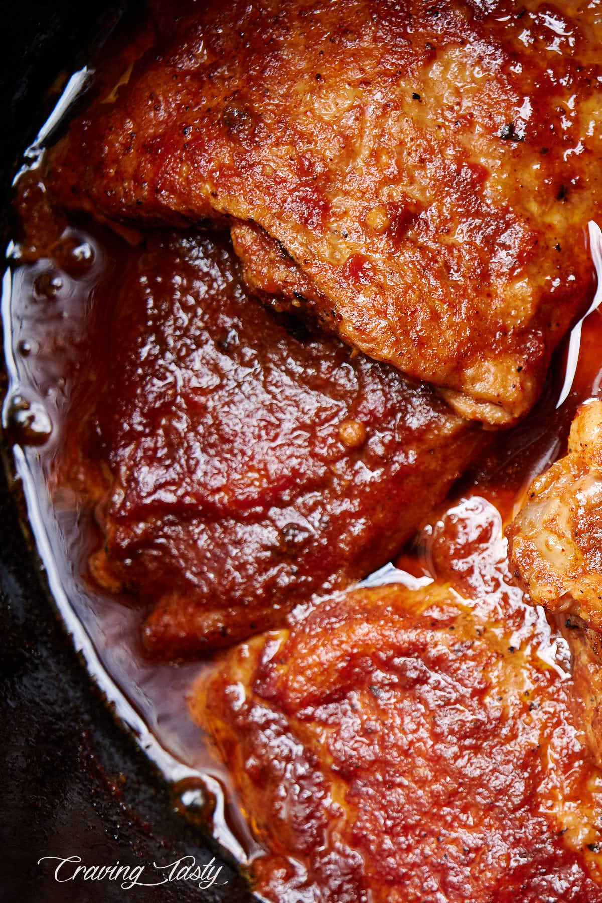 Pieces of chicken covered in BBQ sauce inside a slow cooker.