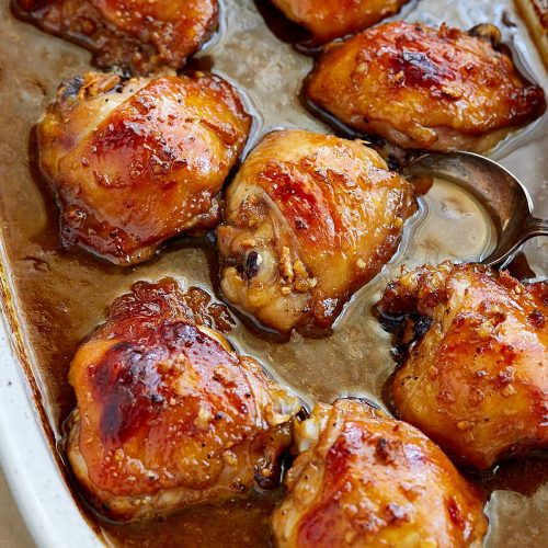 Marinated baked chicken thighs in white baking fish with juices on bottom.