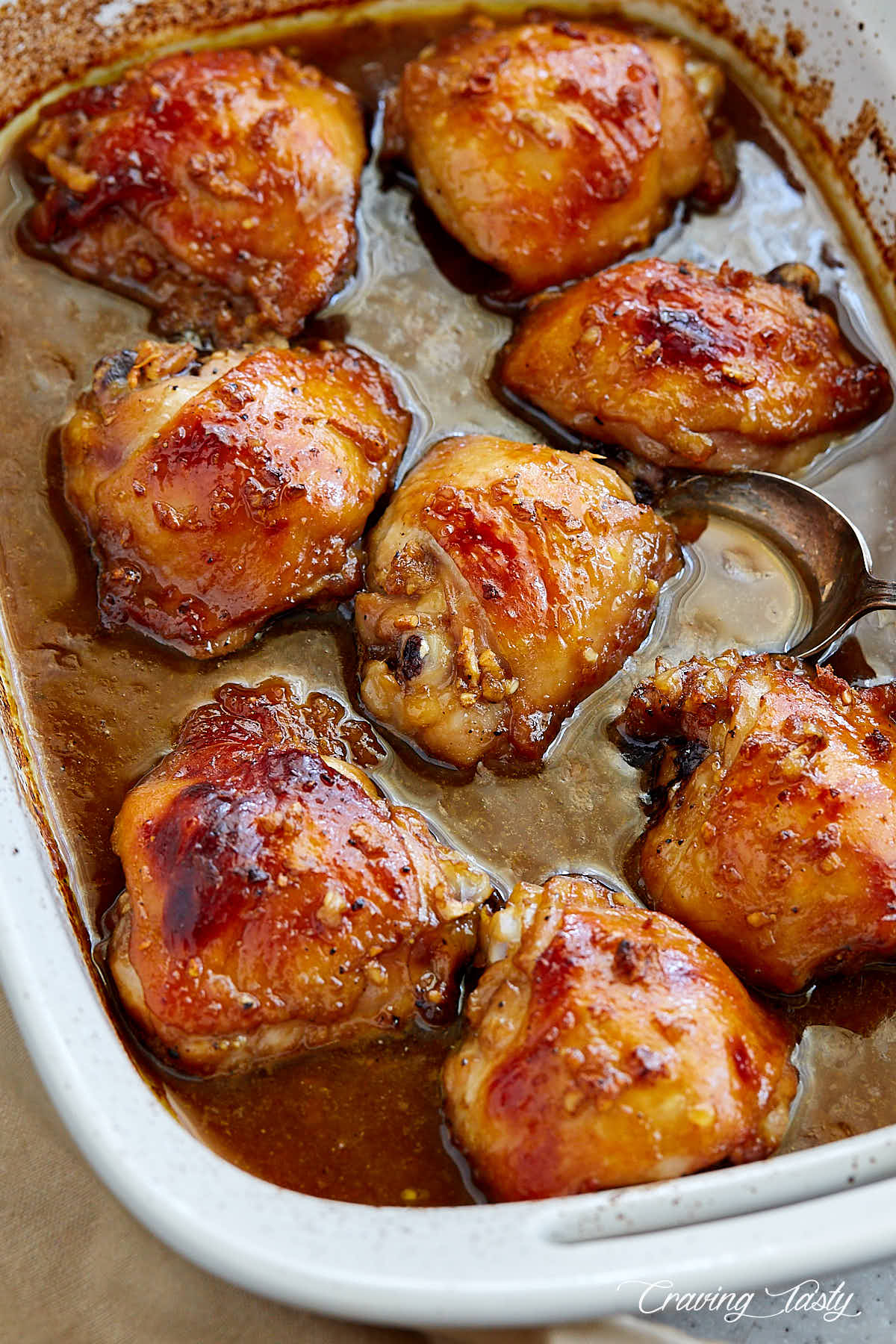 Marinated baked chicken thighs in white baking fish with juices on bottom.