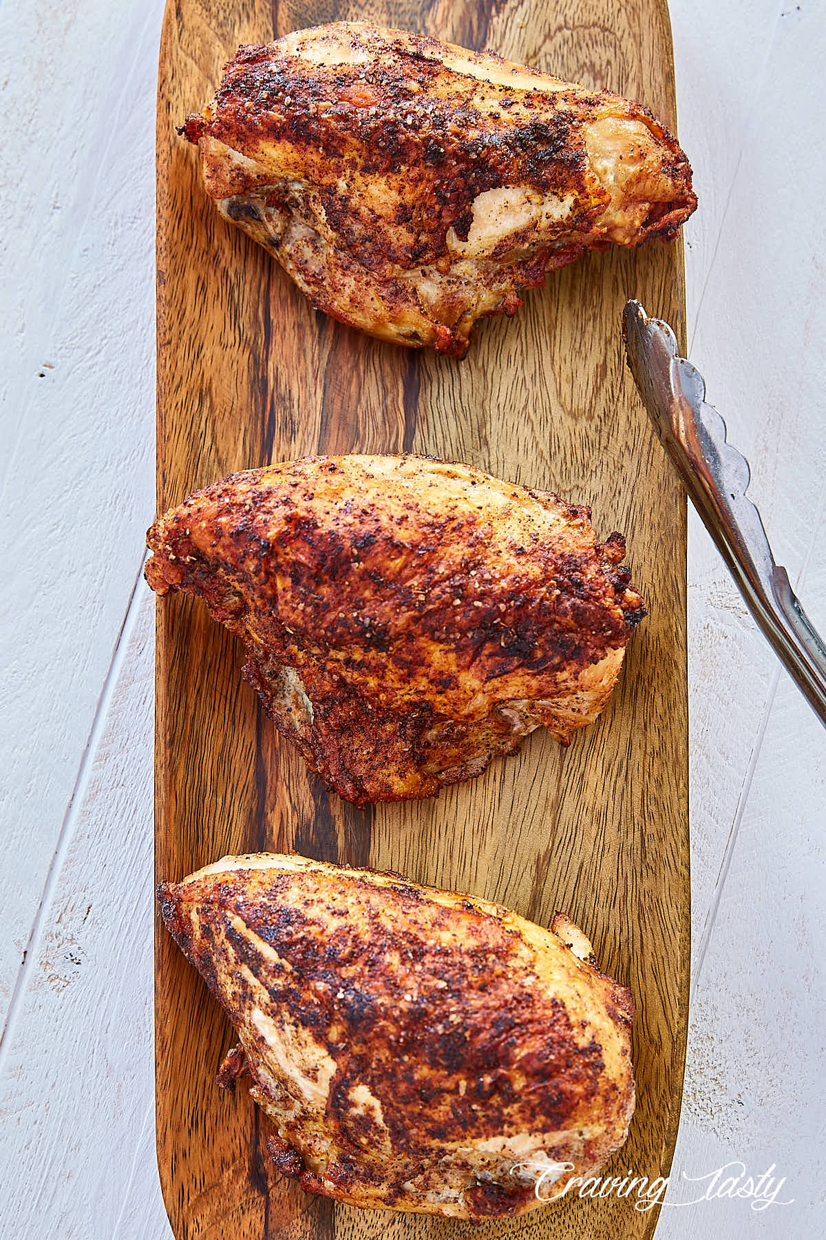 Top down view of three crispy-skinned, tender and juicy oven roasted bone-in chicken breasts on a wooden serving platter.