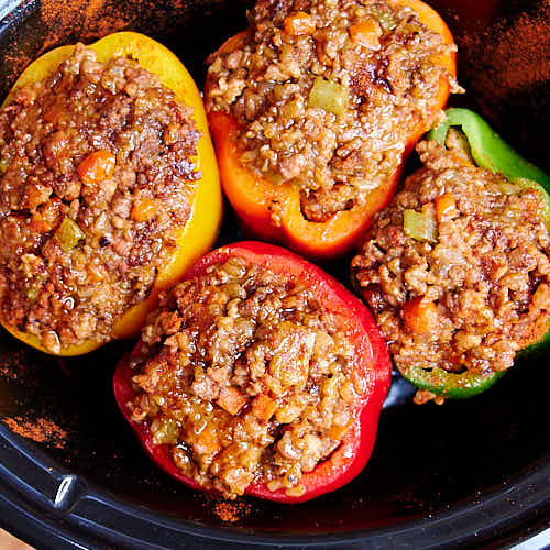 Top down view of colorful bell peppers stuffed with meat and rice stuffing, in a slow cooker.