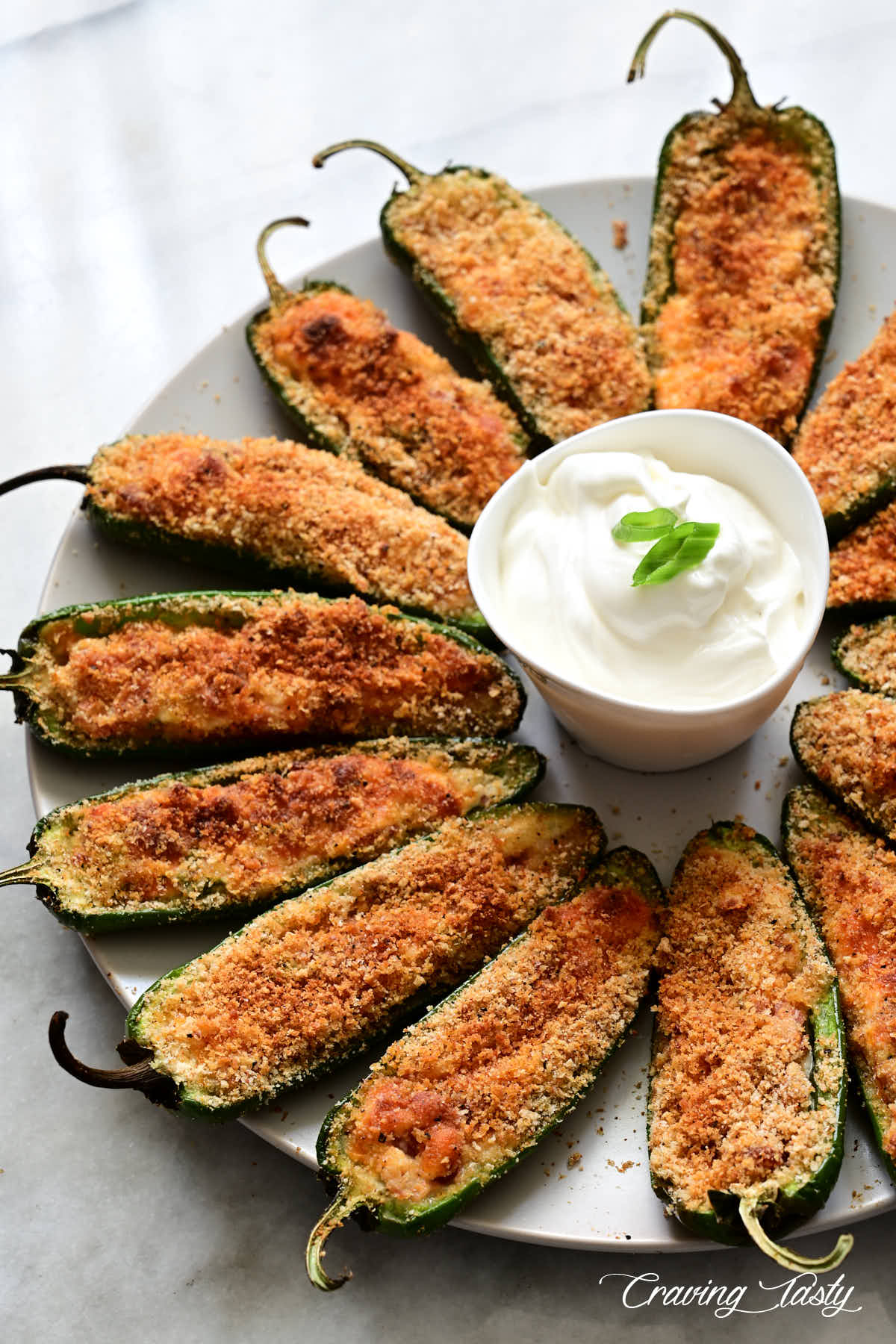 Partial view of a platter with crispy, well-browned jalapeno poppers and a white dipping sauce.