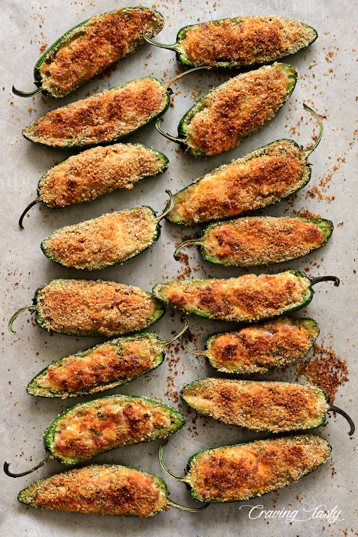 Baked jalapeno poppers with crispy tops on a baking sheet.