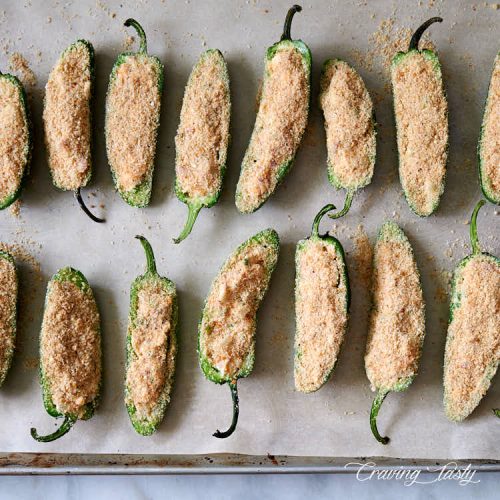 Stuffed jalapeno peppers, dredged in bread crumbs and Parmesan cheese mix, on a baking sheet.