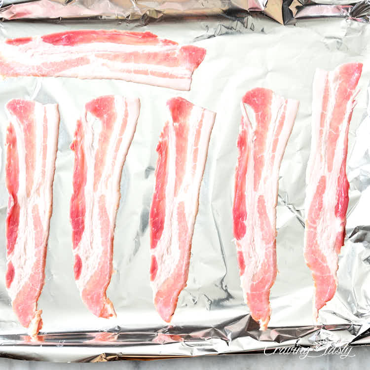 Bacon slices on a baking sheet lined with foil, ready for baking.