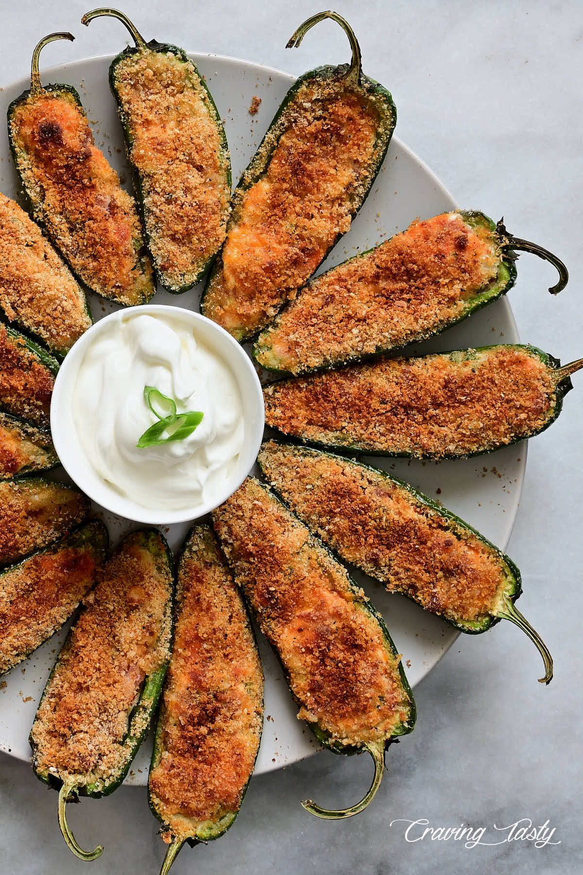 Baked jalapeno poppers on a plate with a saucer with white dipping sauce.