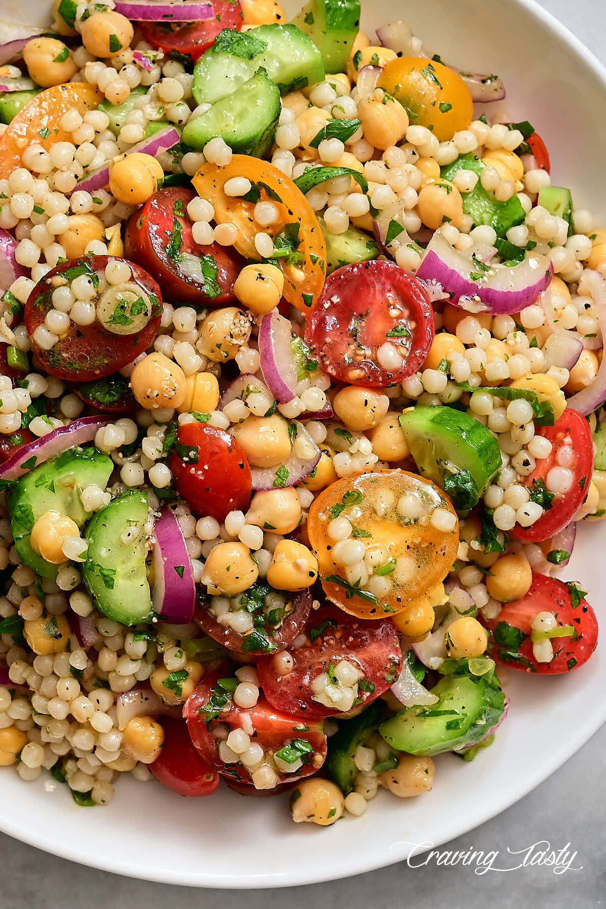 Israeli couscous salad with heirloom tomatoes, cucumbers and herbs on a white plate. 