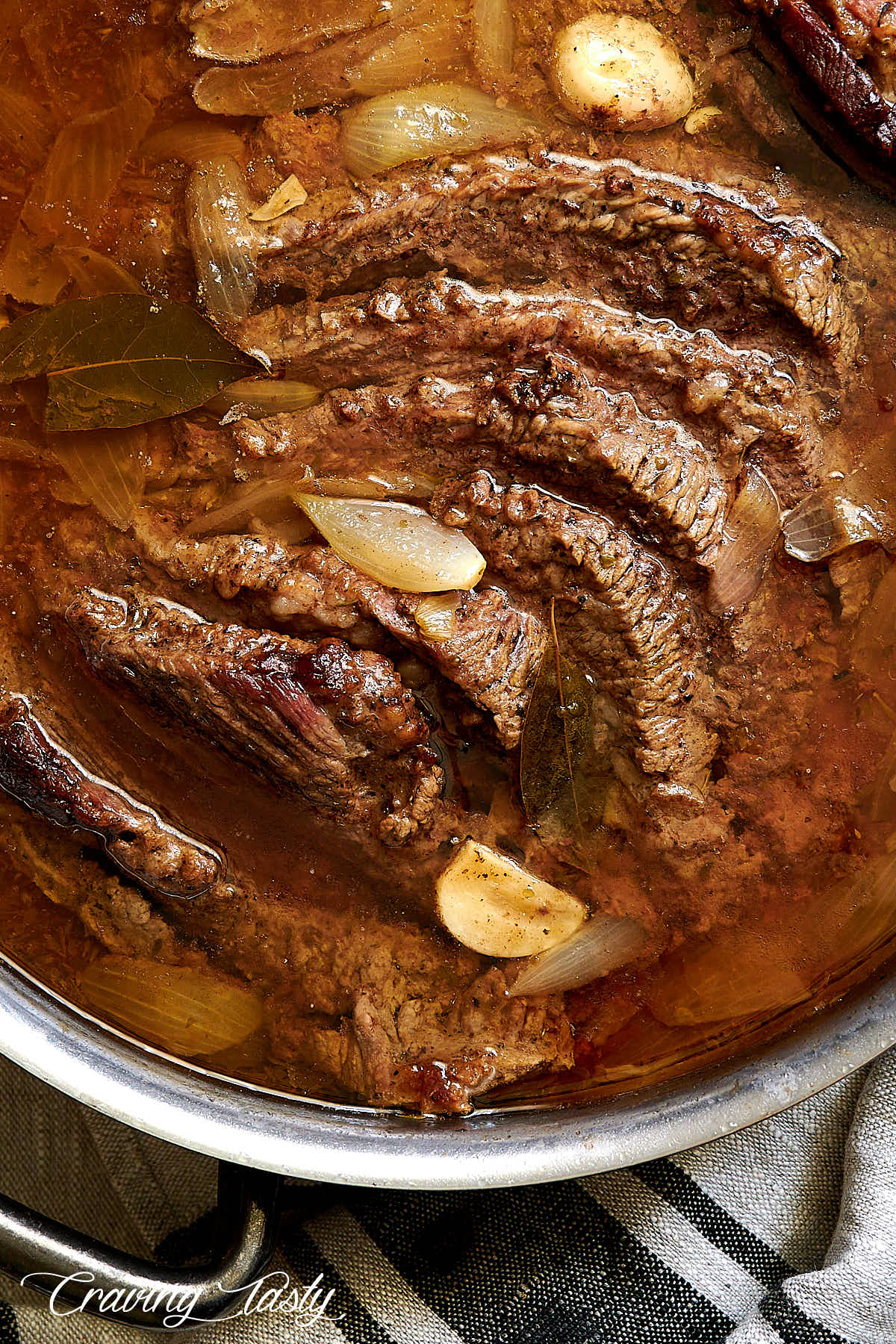 Slices of braised brisket inside of copper braiser covered with amber juices.