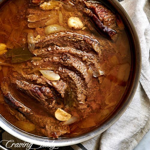 Slices of braised brisket inside of copper braiser covered with amber juices.